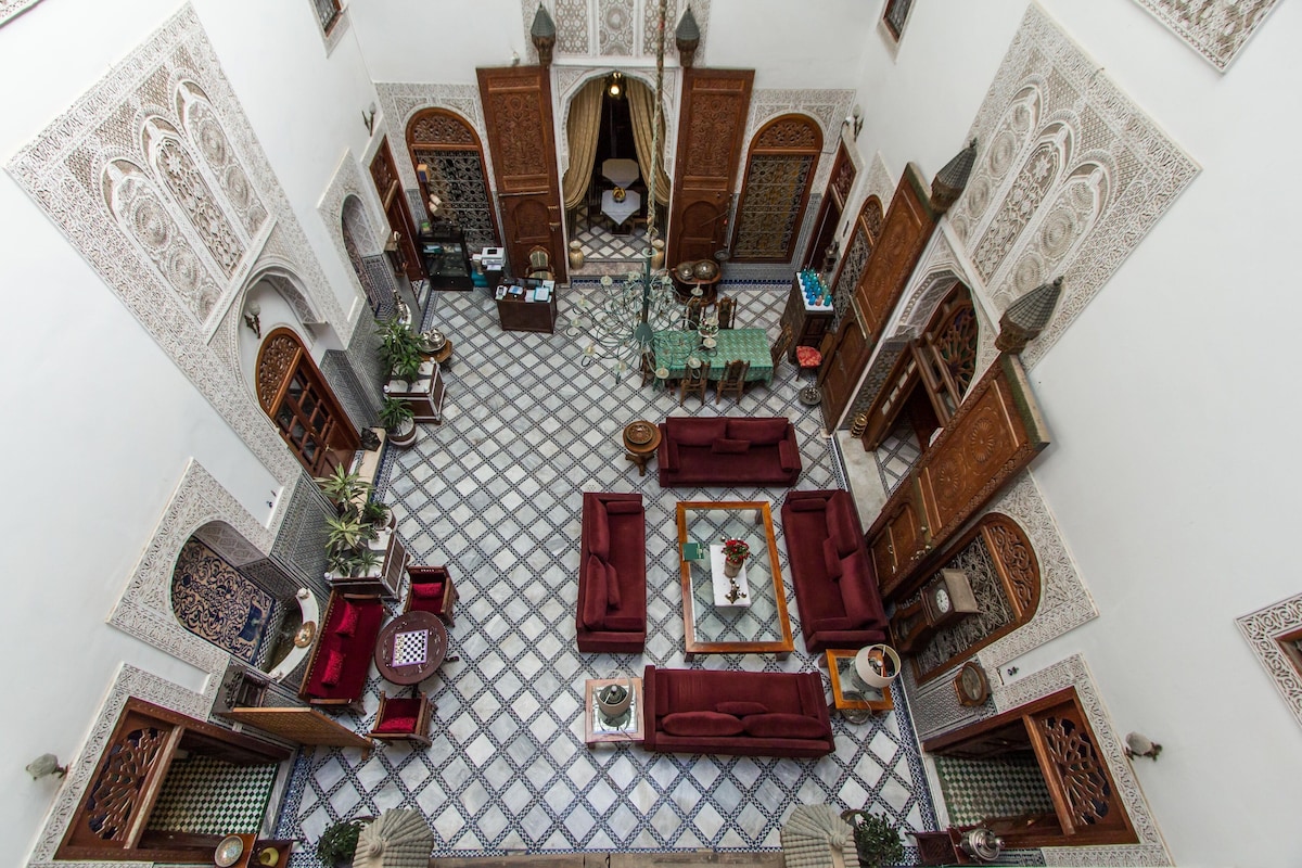 An interior with a tiled floor, red sofas, a central table, and ornate wooden doors.