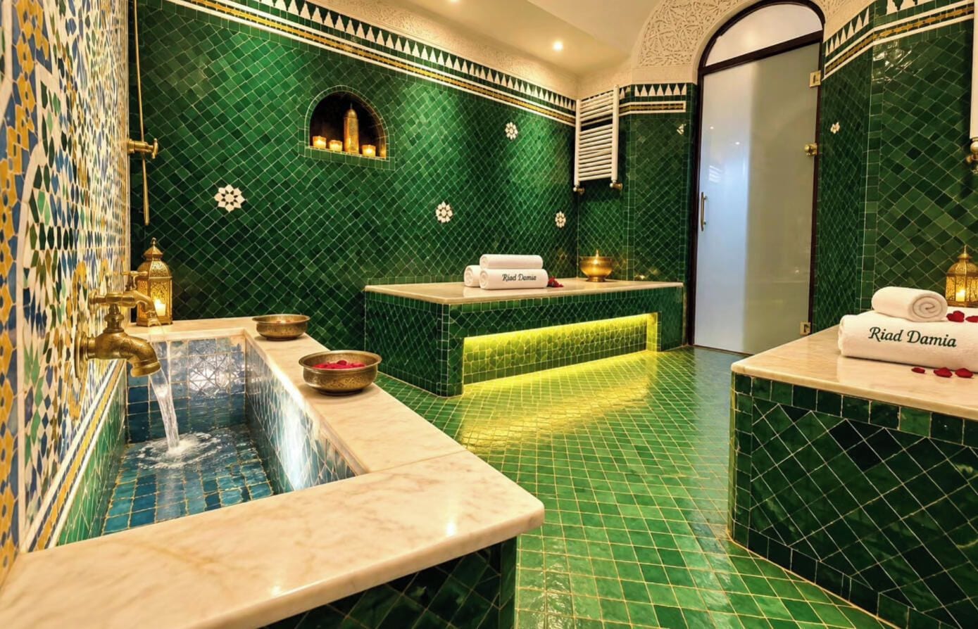 A bathroom with green mosaic tiles, a sink with a gold faucet, and a towel rack with towels.