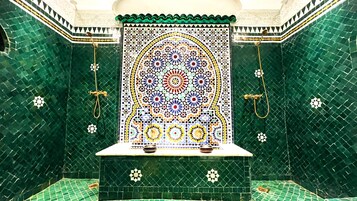 Un baño con mosaicos verdes, un panel decorativo central y dos duchas doradas.