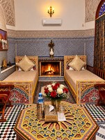 A traditional Moroccan room with a patterned tile wall, a fireplace, two sofas, a coffee table, and a decorative vase.