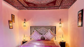 Une chambre avec un lit, deux tables de chevet et un plafond orné de motifs.