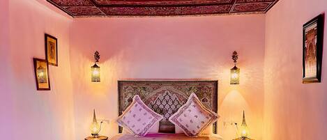 Une chambre avec un lit, deux tables de chevet et un plafond orné de motifs.