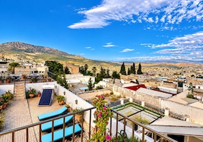 A rooftop terrace with solar panels, outdoor seating, and a view of a cityscape with mountains in the background. - Riad Damia Suite &Spa (Fes)