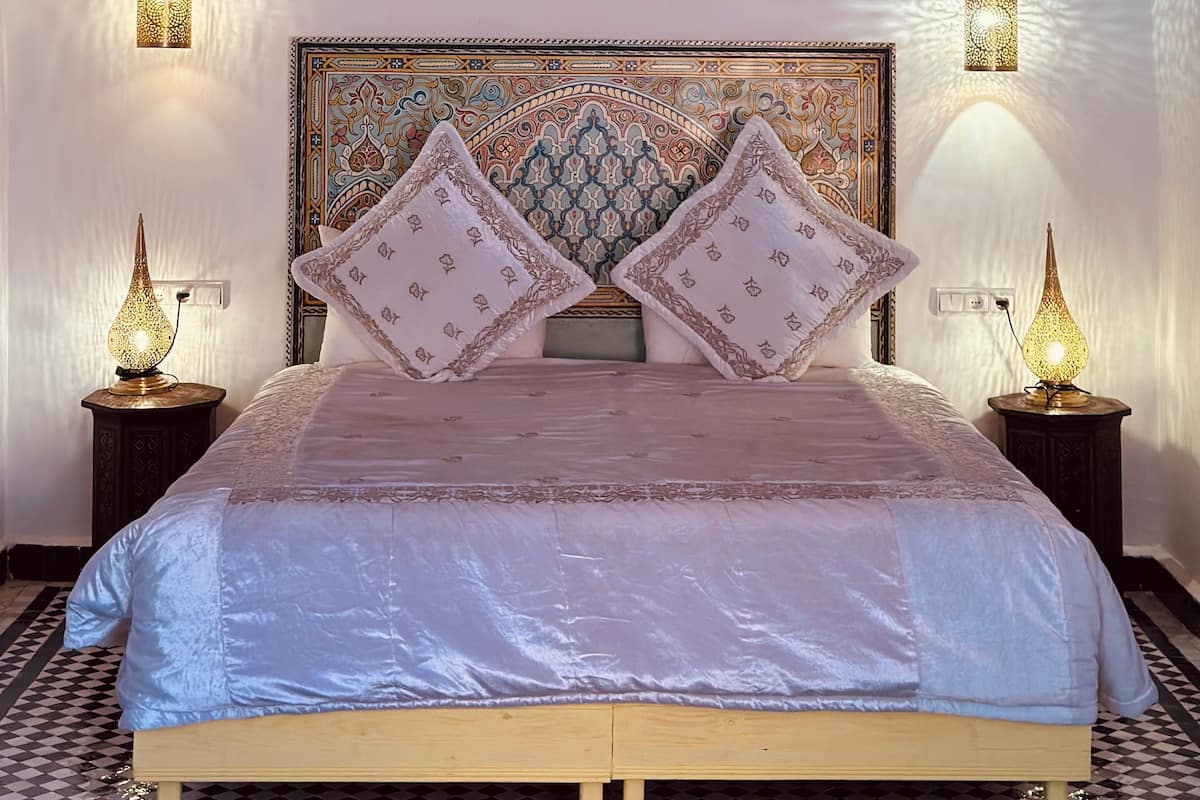 A bedroom with a large bed, ornate headboard, and decorative wall sconces.