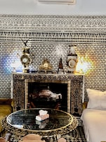 A room with a patterned wall, a fireplace, a table with a tissue box, and a bed.