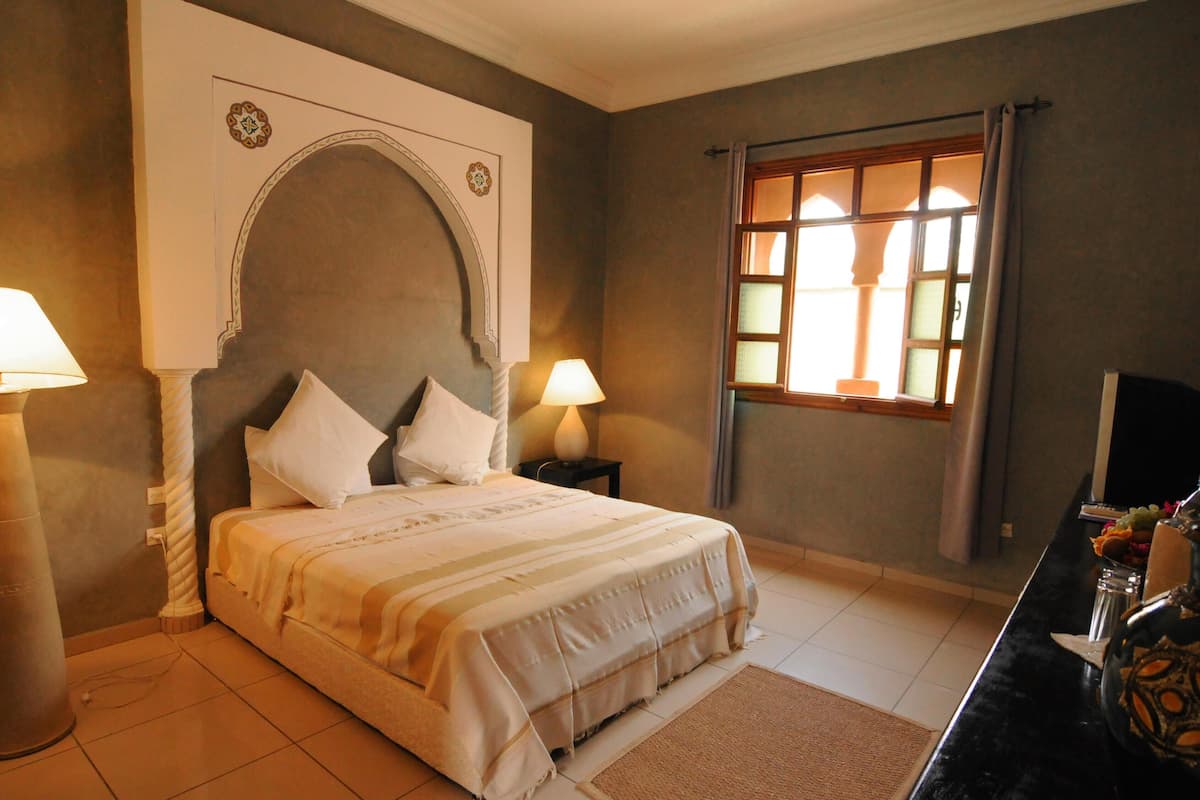 A bedroom with a bed, two bedside lamps, a window with curtains, and a television on a stand.