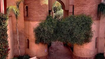 Un patio con un arco central, rodeado de edificios de ladrillo con techos abovedados, un banco y plantas en macetas.