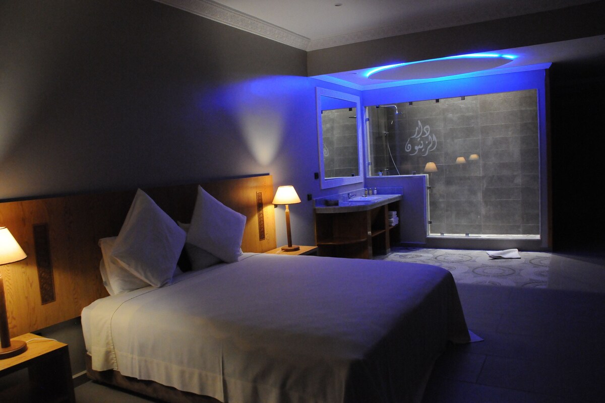 Une chambre d’hôtel avec un lit, des lampes de chevet, une coiffeuse avec un miroir et une fenêtre donnant sur un paysage agréable.