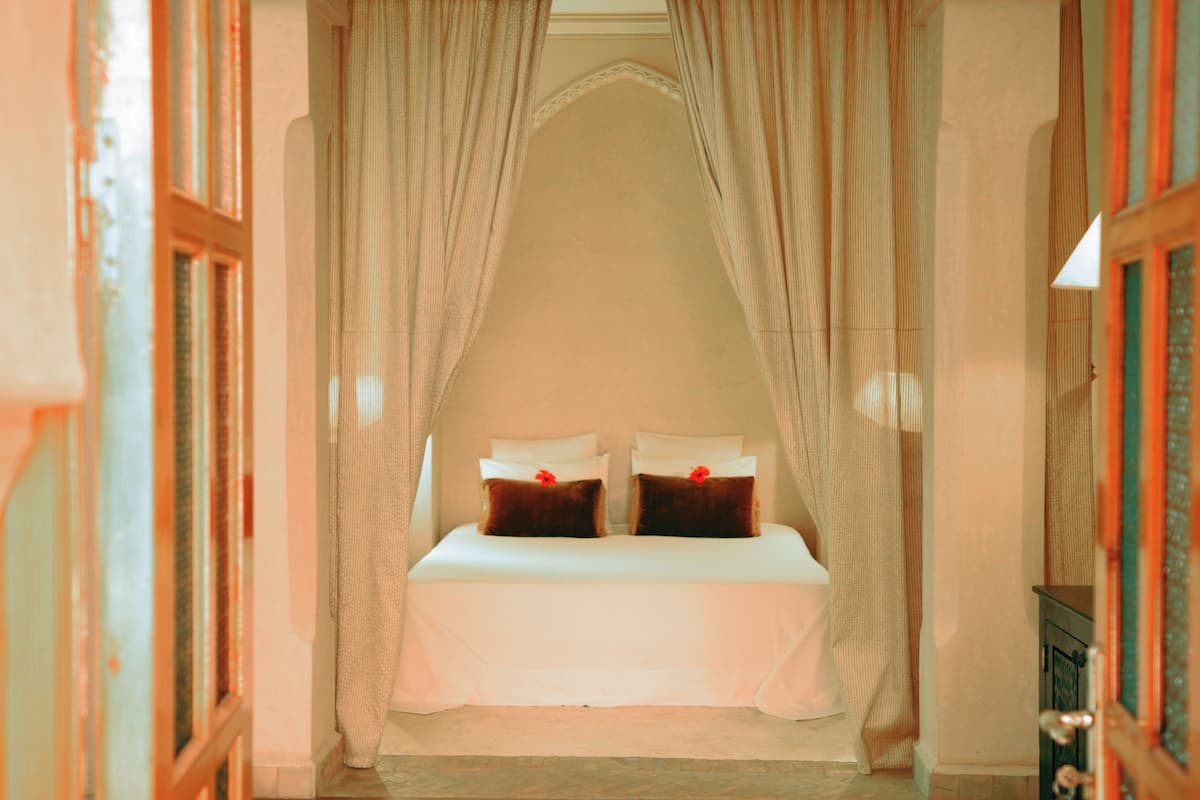 A room with a bed under a canopy, a door on the left, and a wall on the right.