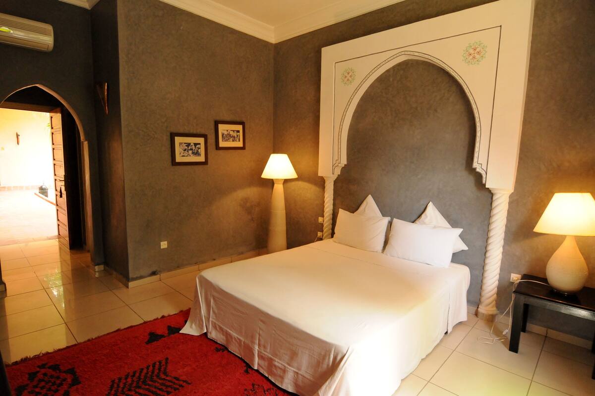 Une chambre d’hôtel avec un grand lit, deux lampes de chevet, un tapis rouge et une arche décorative au-dessus du lit.
