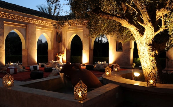 Un espacio de comedor al aire libre con arcos, piscina y faroles decorativos.