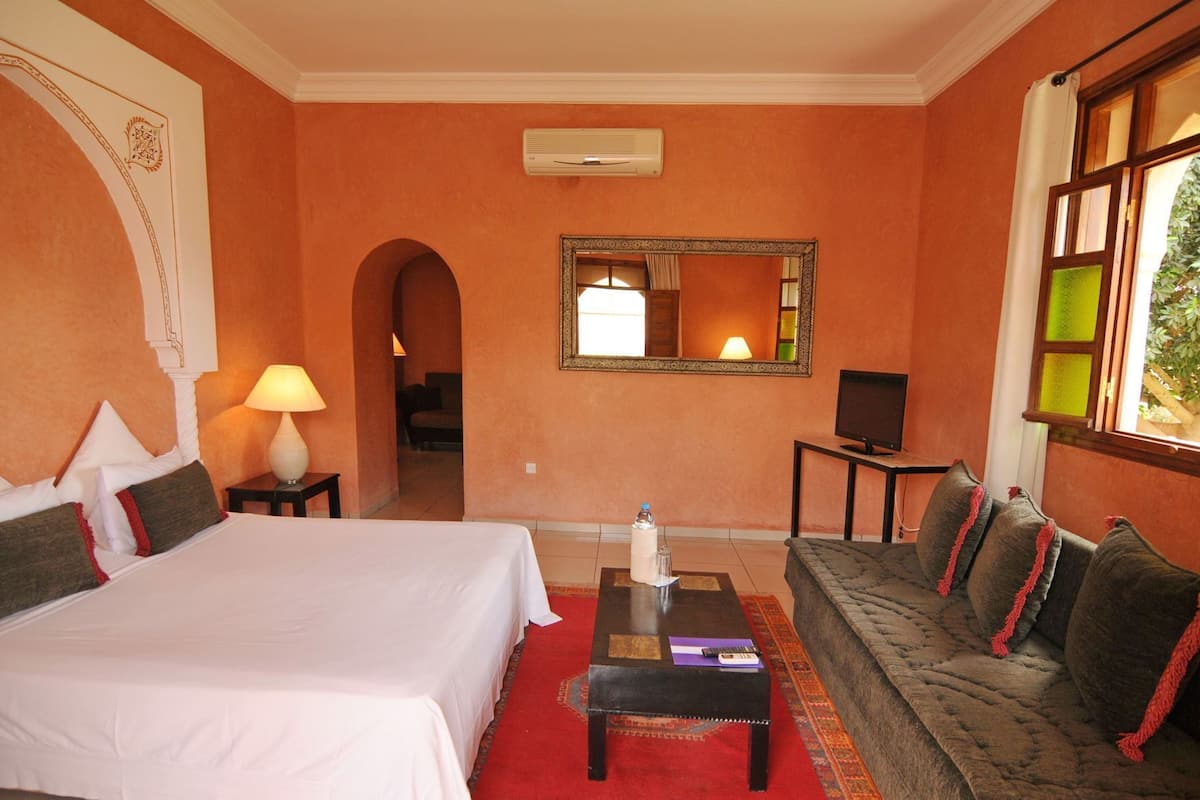 Une chambre d’hôtel avec un grand lit, un canapé, une télévision et un miroir au mur.