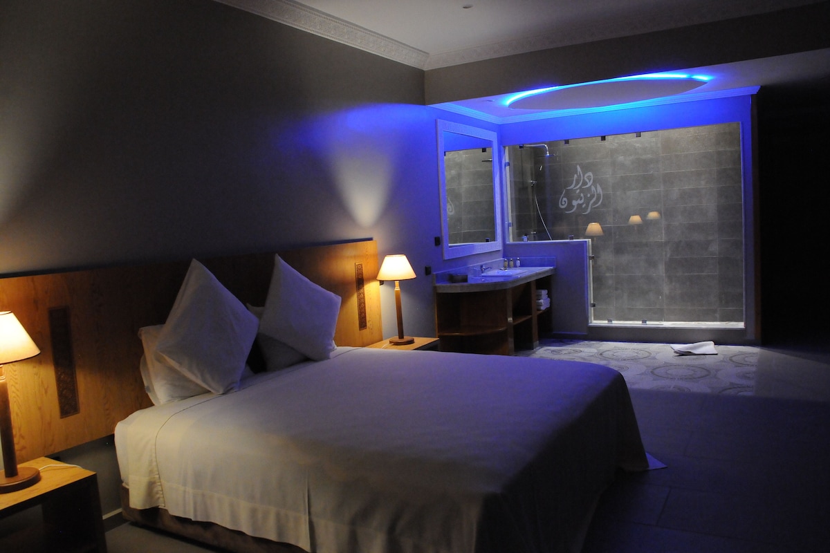 A hotel room with a bed, bedside lamps, a vanity with a mirror, and a window with a view.