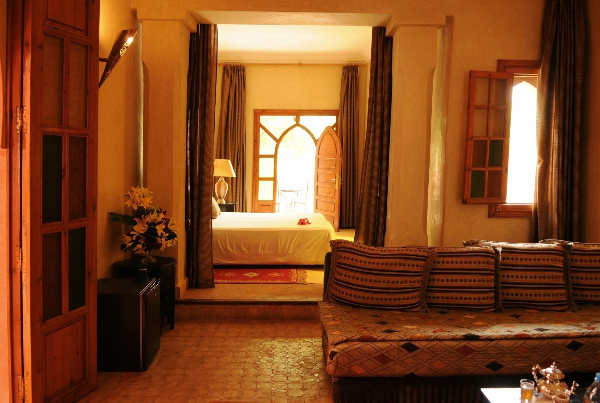 Una habitación acogedora con cama, sofá, una mesita con lámpara y ventana con cortinas.