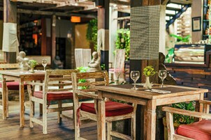 A restaurant with wooden tables and chairs, a checkered cloth hanging, and a display case in the background.