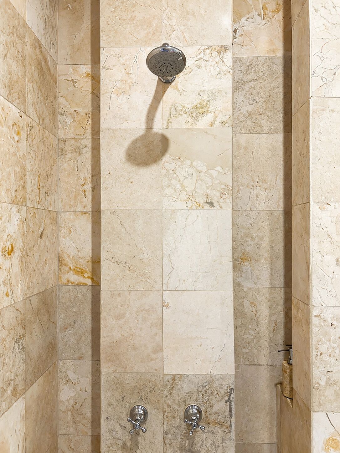 Ducha con cabezal de ducha de mano, grifo empotrado en la pared y suelo de azulejos.