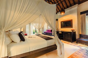 A bedroom with a canopy bed, a television mounted on the wall, and a seating area with a bench and a sofa.