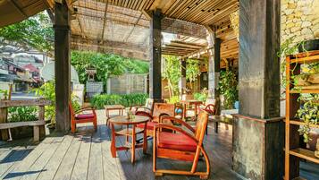 Una terraza exterior de madera con mesas y sillas, rodeada de vegetación y muros de piedra.