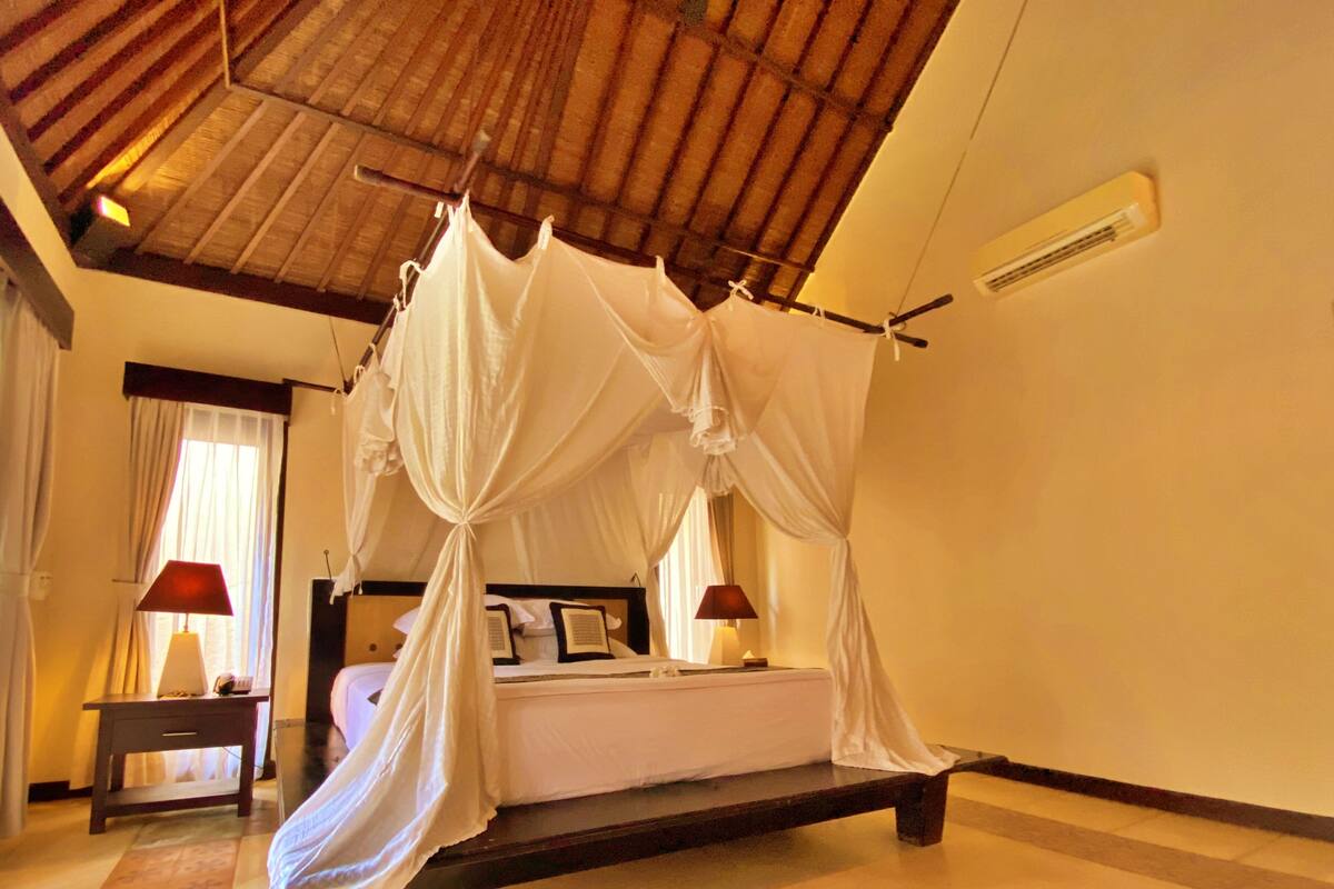 A four-poster canopy bed in a room with a wooden ceiling and a tiled floor.