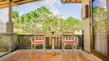 Un patio cubierto con una mesa y sillas, un muro de piedra y vistas a árboles y edificios.