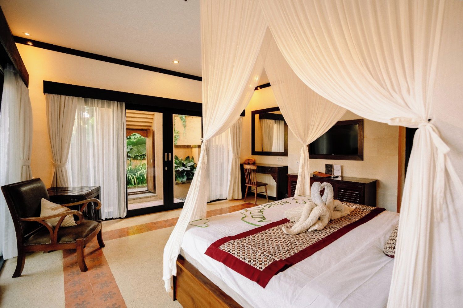 A bedroom with a canopy bed, a desk, a chair, and a view of greenery outside.