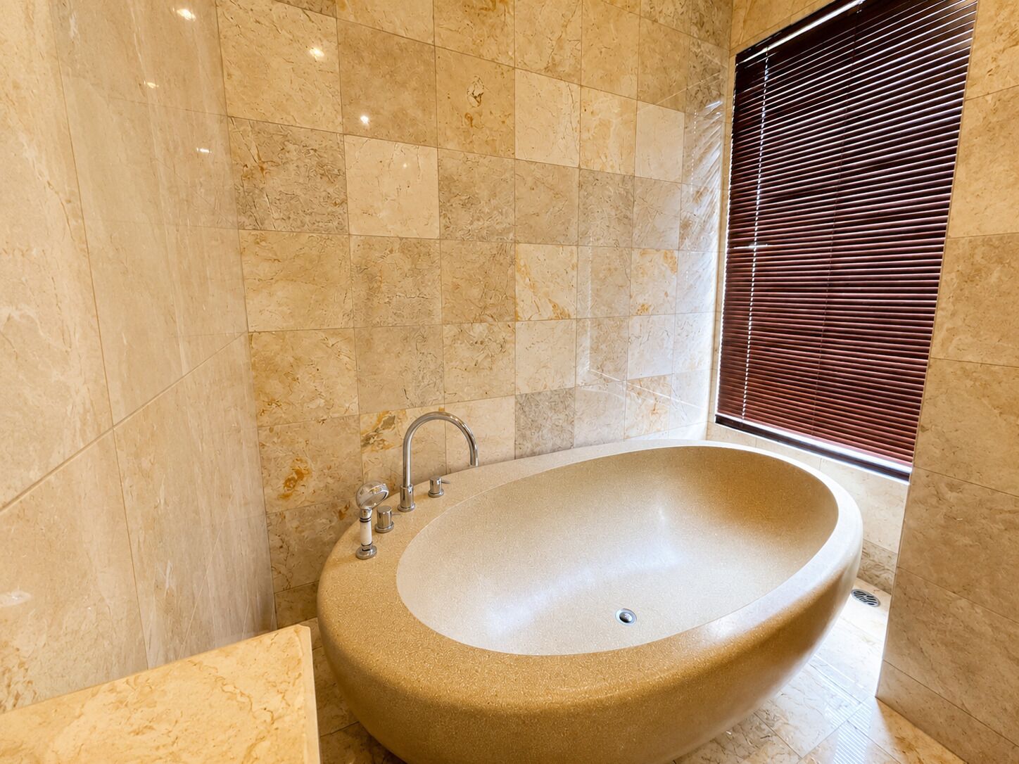 A bathroom with a freestanding bathtub, tiled walls, and a window with blinds.