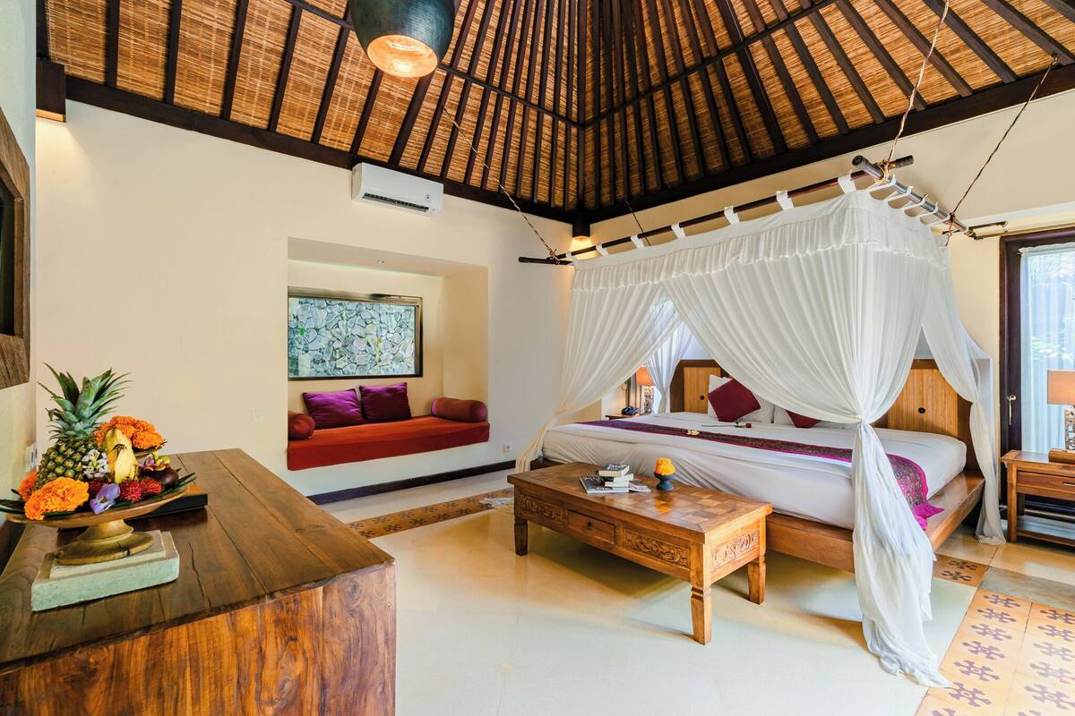 A room with a bed under a canopy, a wooden coffee table, a sofa, and a wall-mounted air conditioner.