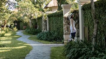 A pathway lined with hedges and a statue, leading to a building with a thatched roof.
