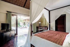 A bedroom with a large bed, a television, and a desk. There is a view of an outdoor area with a bench and greenery. - Kayumanis Sanur Private Villa & Spa (Denpasar)