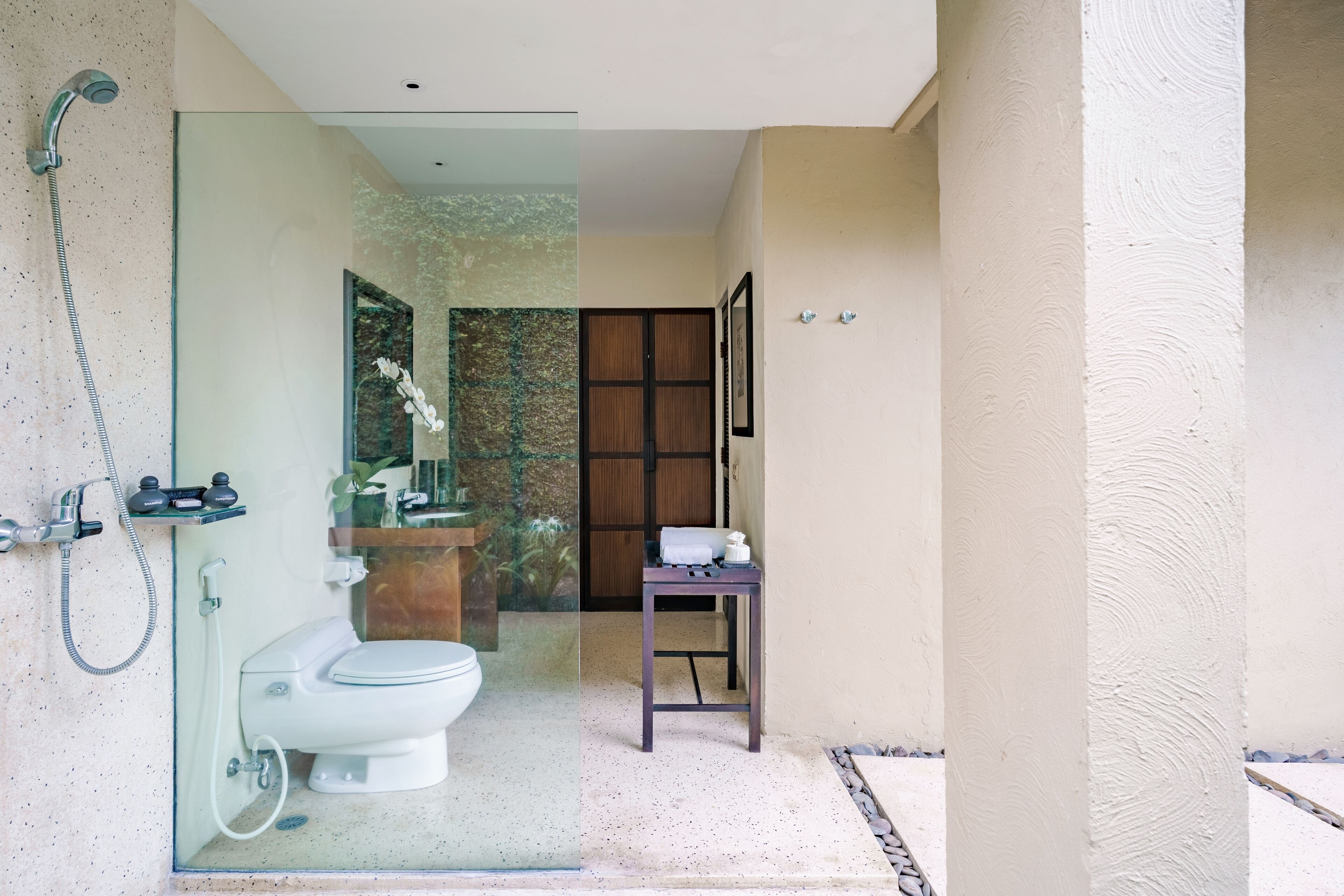 A modern bathroom with a glass partition, a shower, a toilet, and a small table with toiletries.