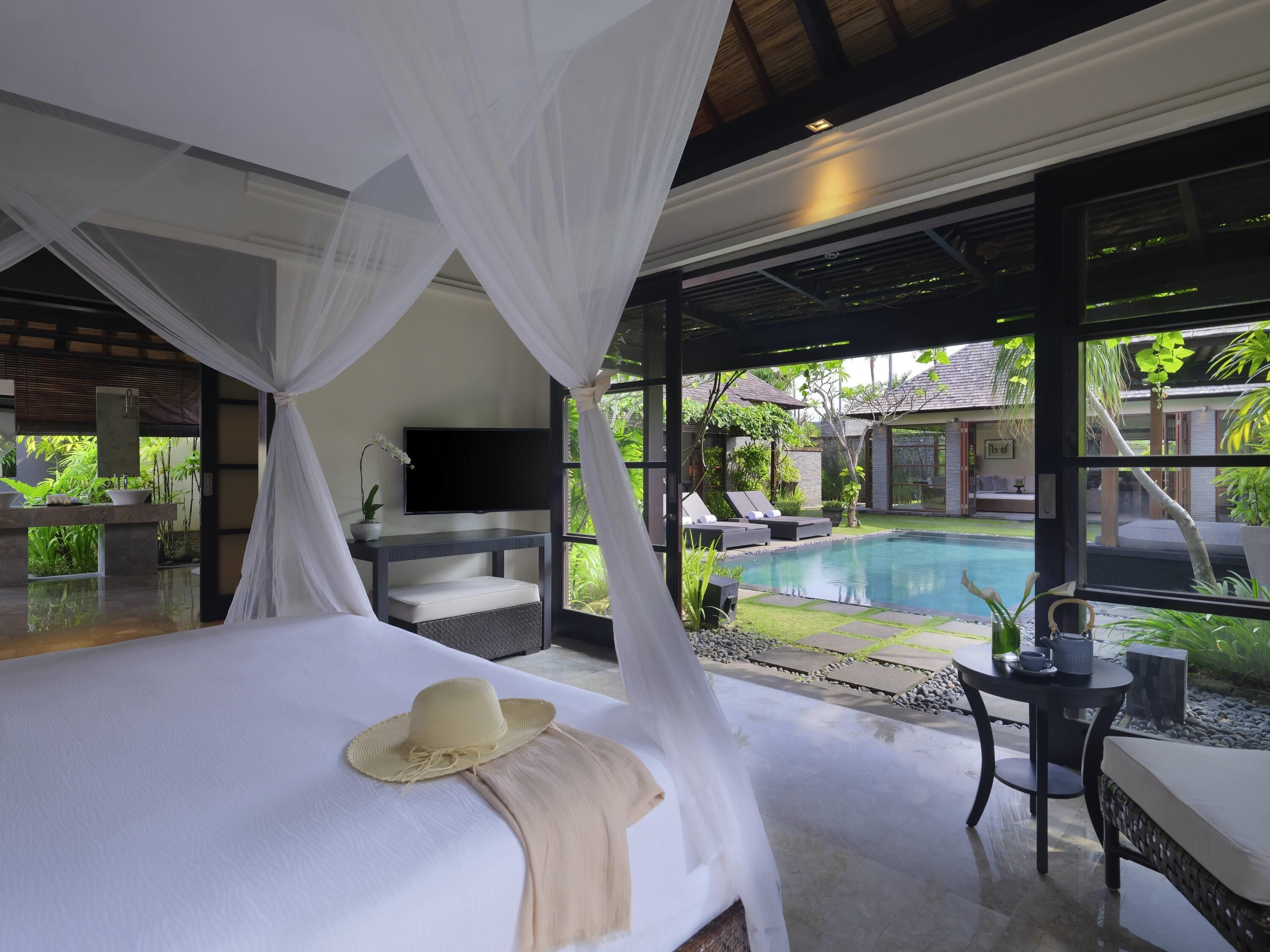 Ein Schlafzimmer mit Bett, Fernseher, einem kleinen Tisch und Blick auf einen Swimmingpool.