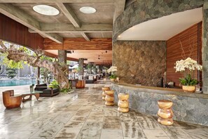 Un hall d’entrée spacieux avec un mur en pierre, un plafond en bois et une vue sur la piscine.