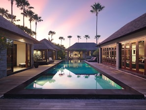 A poolside view of a resort with multiple overwater bungalows, a clear pool, and palm trees. - Peppers Seminyak (Seminyak)