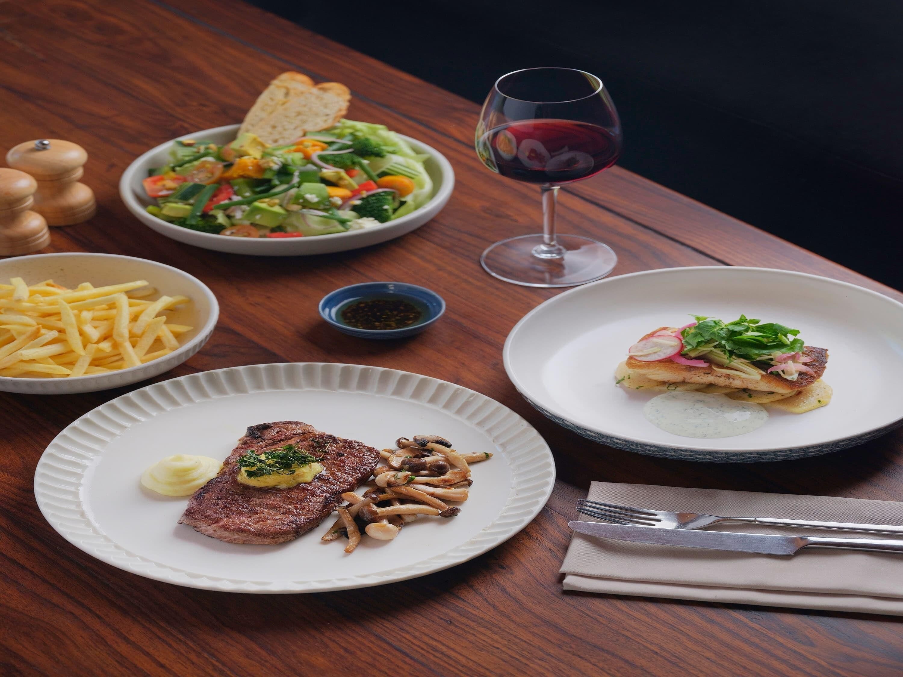 Une table à manger avec différents plats, notamment un steak, des champignons et une salade.