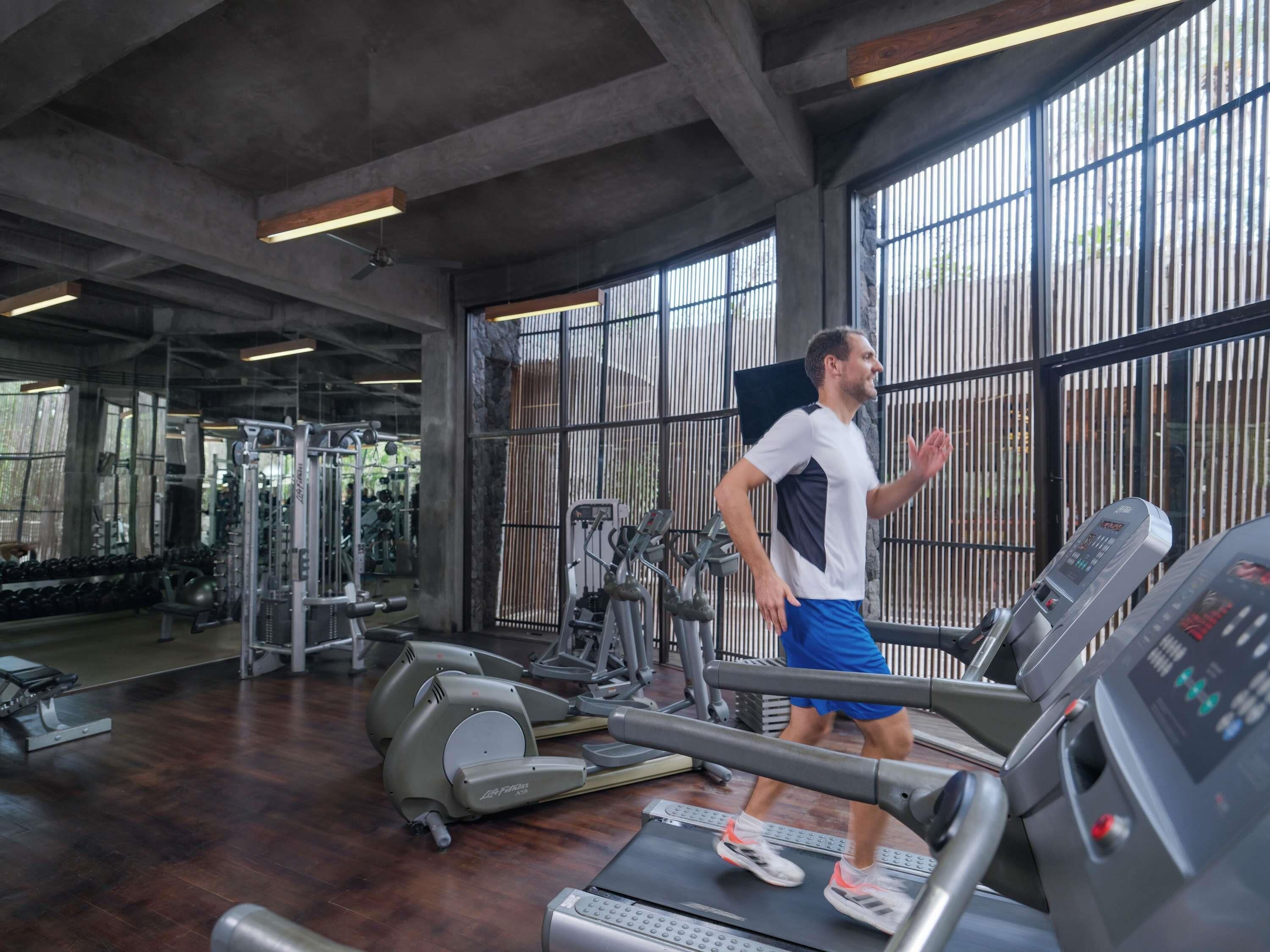 Een sportschool met trainingsapparatuur, grote ramen en een betonnen plafond.
