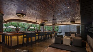 A bar area with a counter, bar stools, and a seating area with sofas and a coffee table. - Peppers Seminyak (Seminyak)