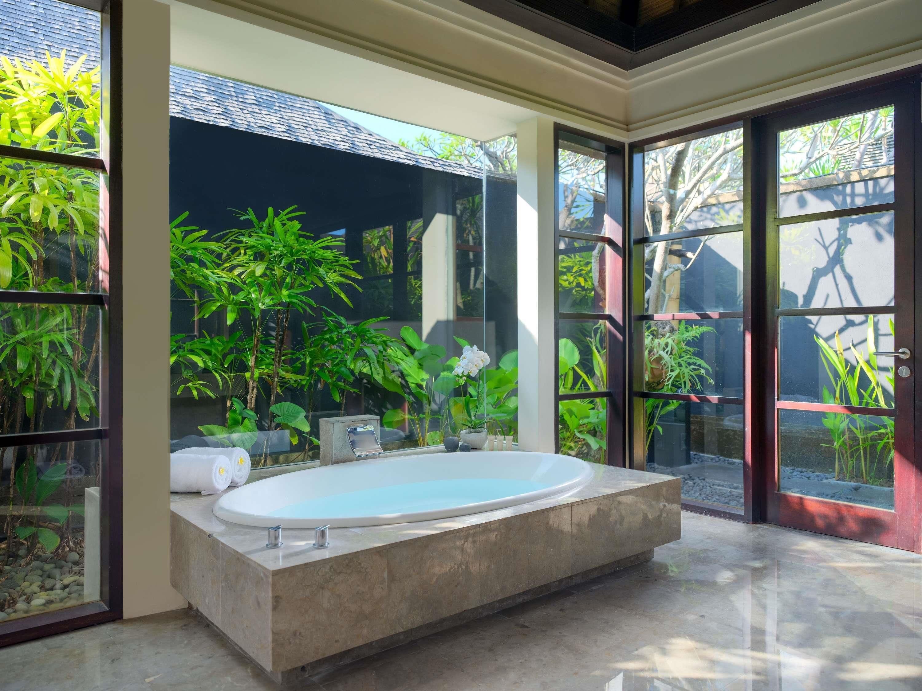 A modern bathroom with a freestanding bathtub, large windows, and lush indoor plants.