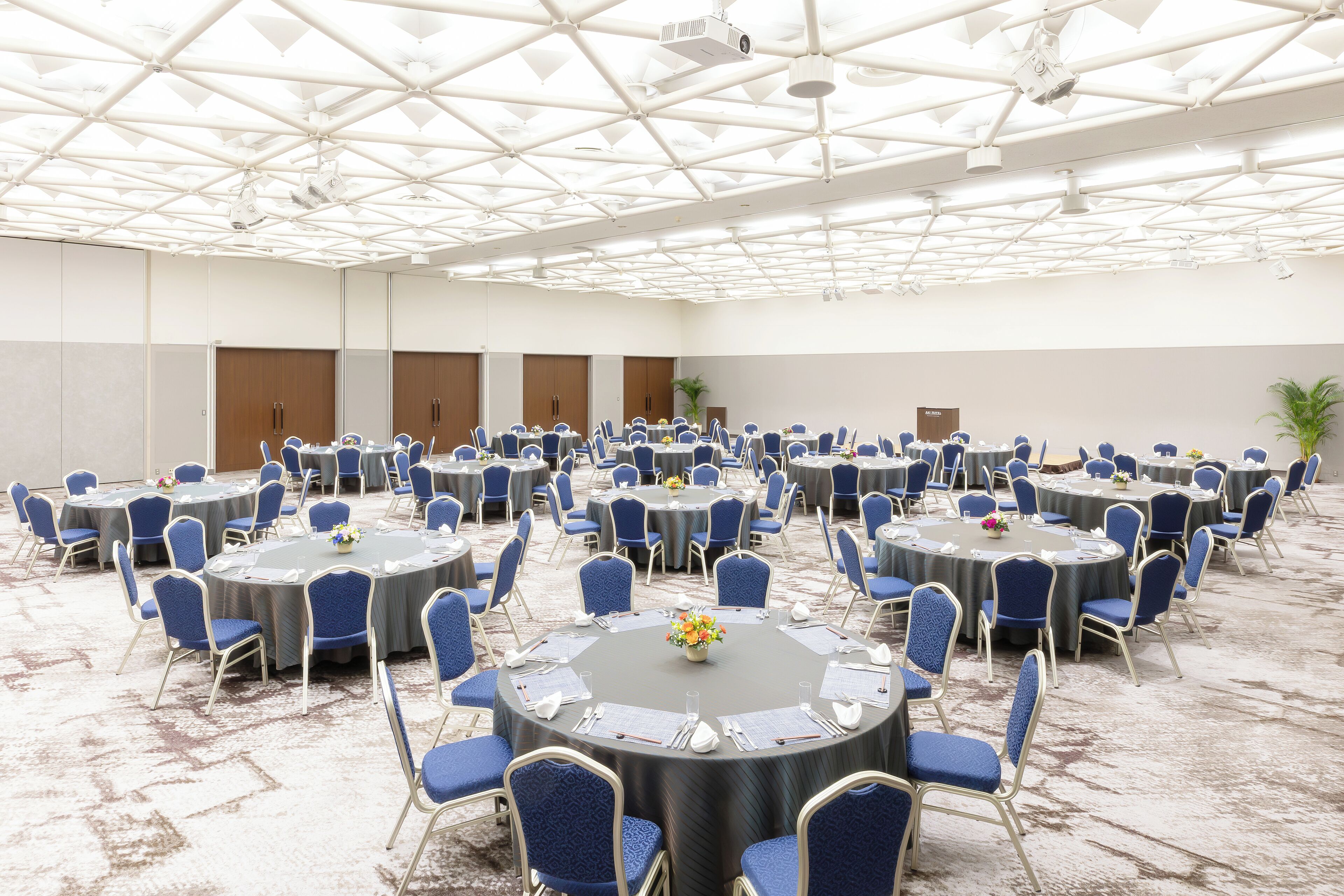 A conference room with round tables and blue chairs, arranged in a grid pattern.