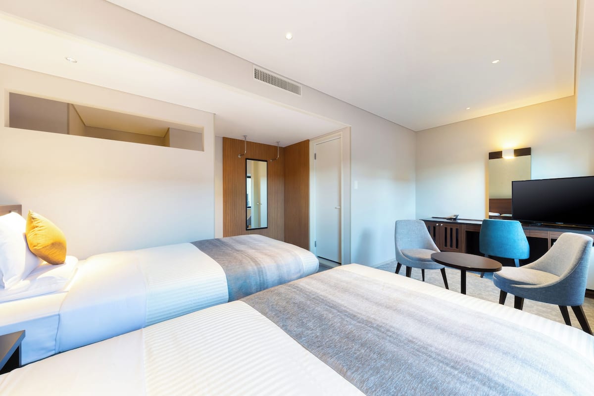 Ein Hotelzimmer mit zwei Betten, einem Schreibtisch mit Stuhl, einem Fernseher und einem Spiegel.