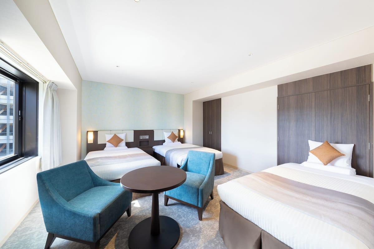 Ein Hotelzimmer mit zwei Betten, einem kleinen Tisch, einem blauen Sessel und einem großen Fenster.
