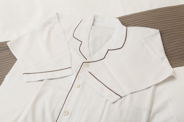 Una camisa blanca impecablemente doblada con ribetes y botones marrones, sobre una superficie a rayas.