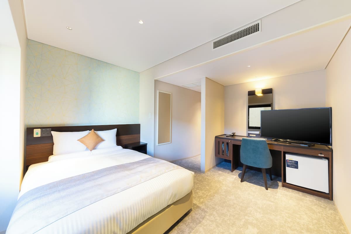 Ein Hotelzimmer mit einem Bett, einem Schreibtisch, einem Fernseher und einem kleinen Kühlschrank.