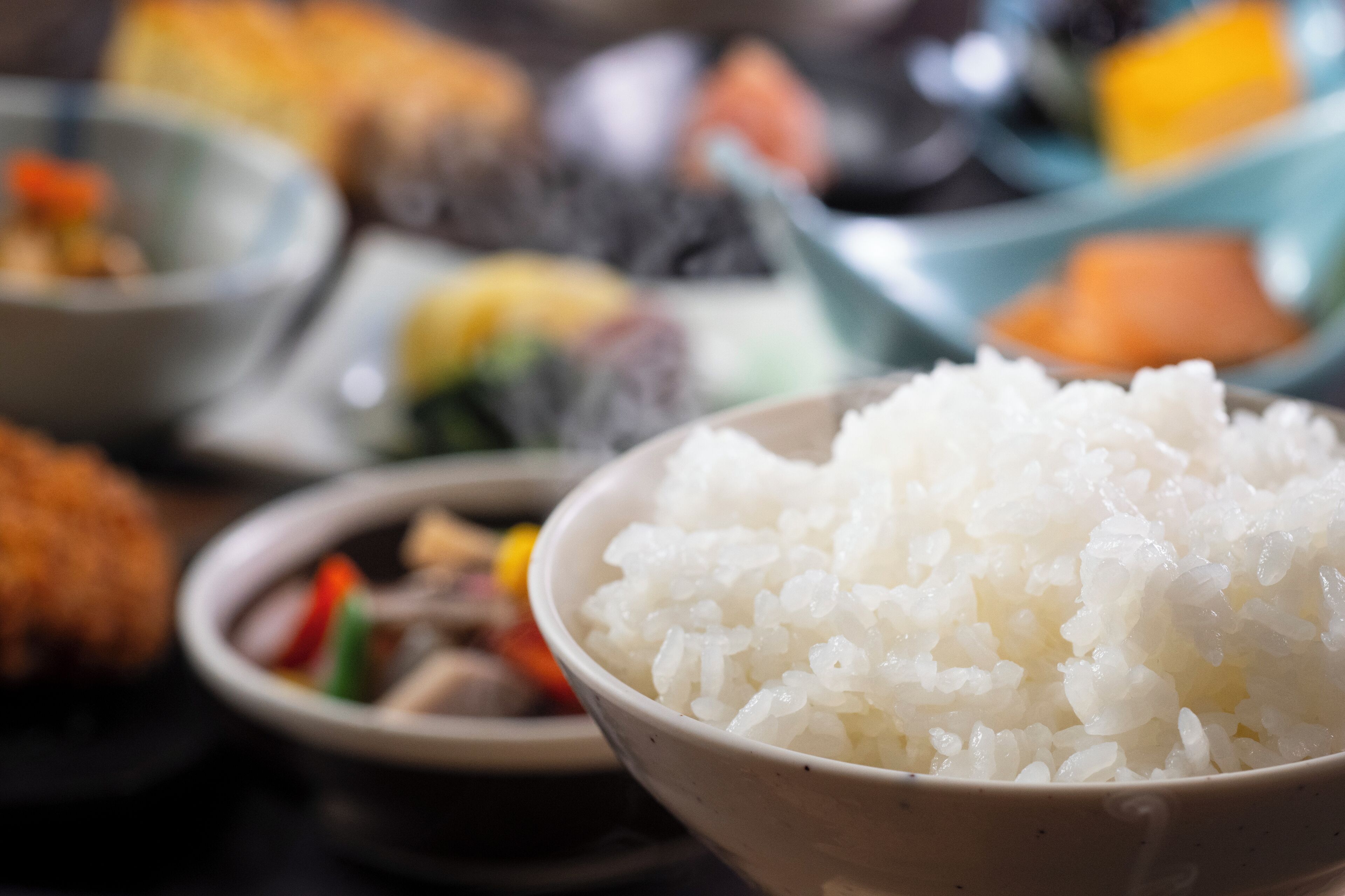 Un tazón de arroz blanco en primer plano, con platos desenfocados al fondo.