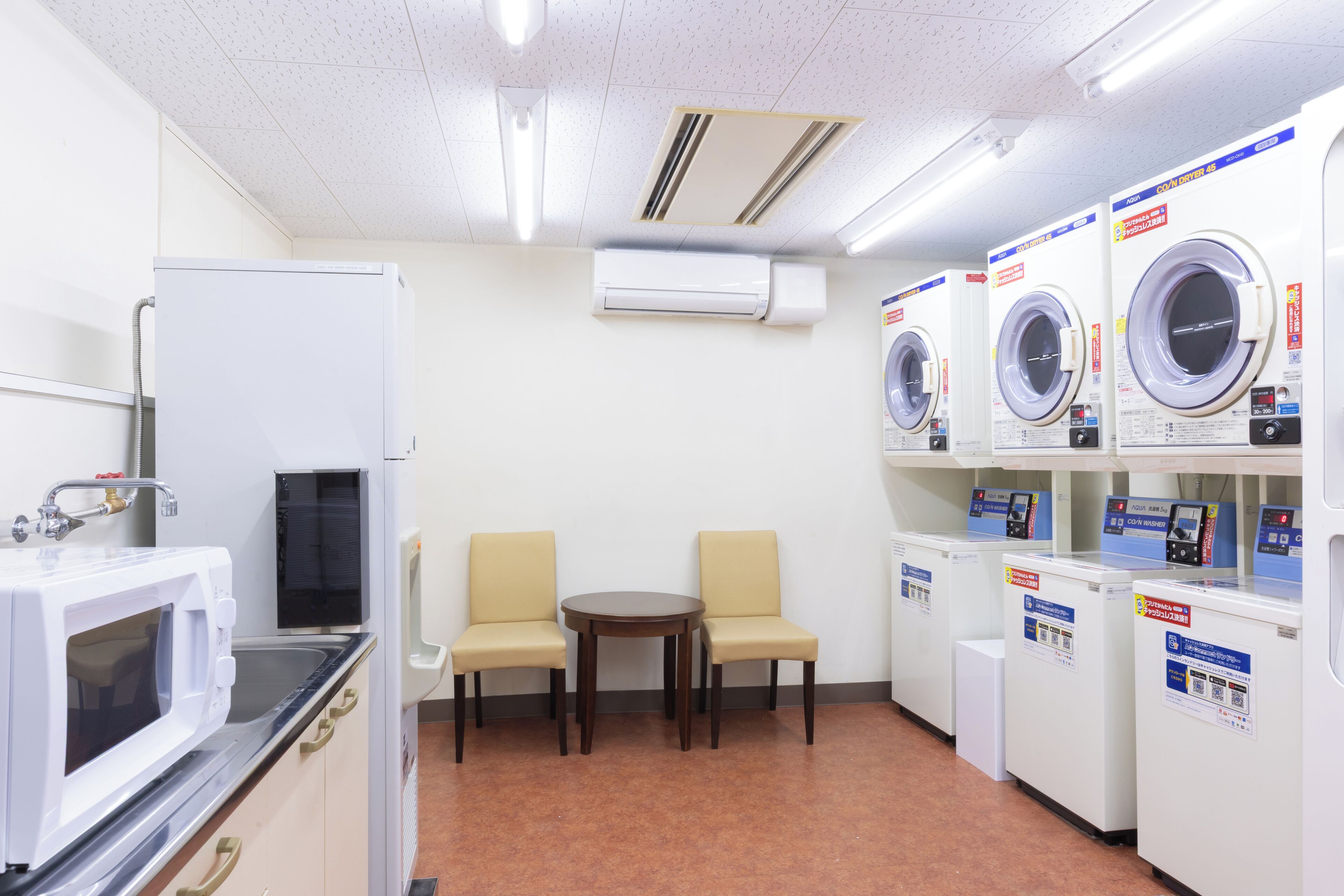 A laundry room with washing machines, a microwave, and two chairs.