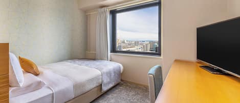 A hotel room with a bed, a desk, a television, and a window with a city view.