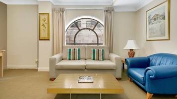 Una sala de estar con un sofá color beige, un sofá azul, una mesa de centro de madera y un amplio ventanal abovedado con cortinas.