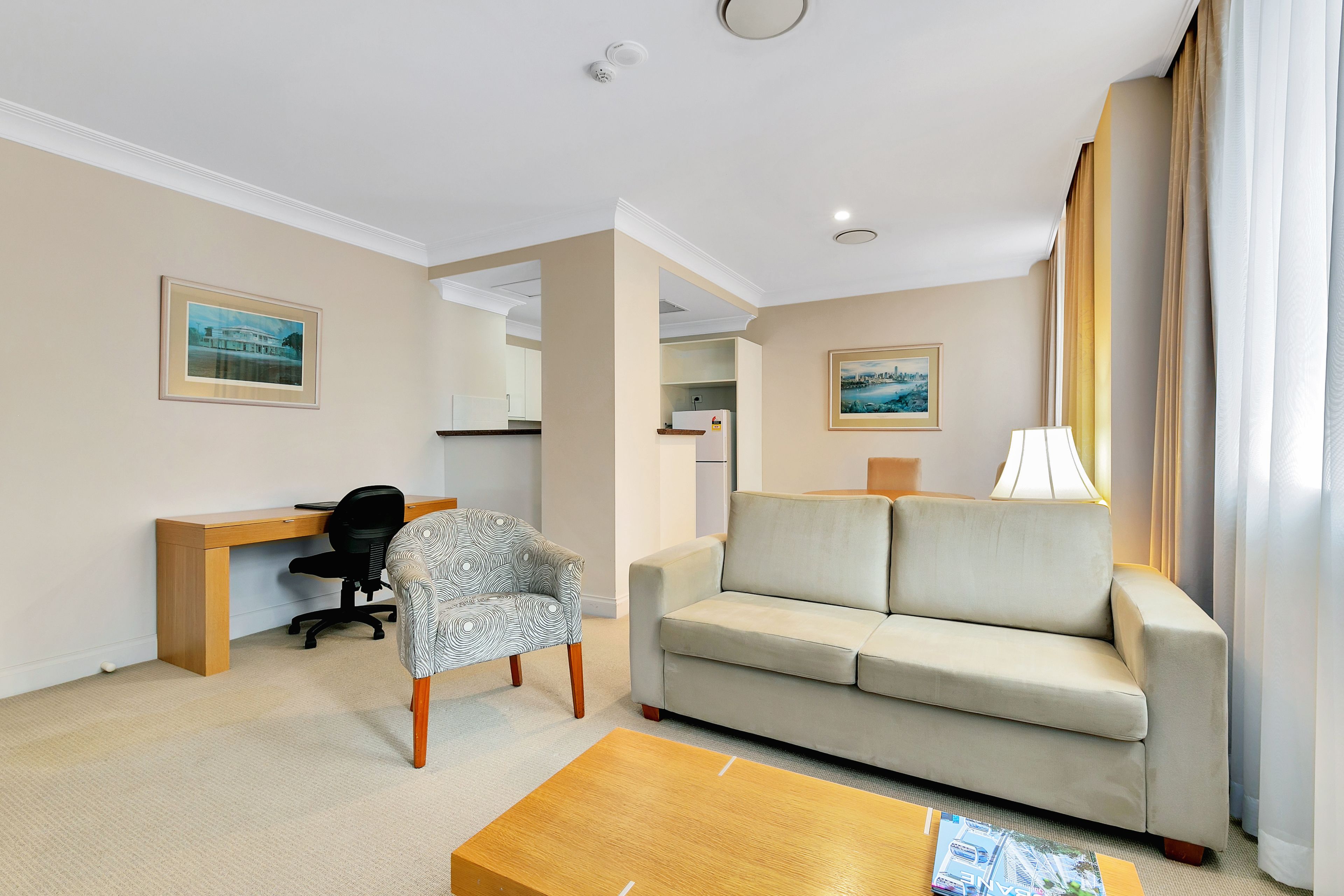 A hotel room with a beige sofa, a wooden desk, a patterned armchair, and a coffee table.