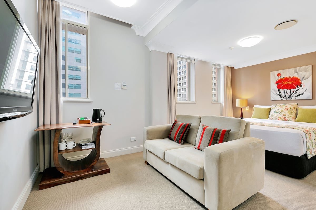 Habitación de hotel con sofá, cama, televisor, cafetera y un cuadro en la pared.
