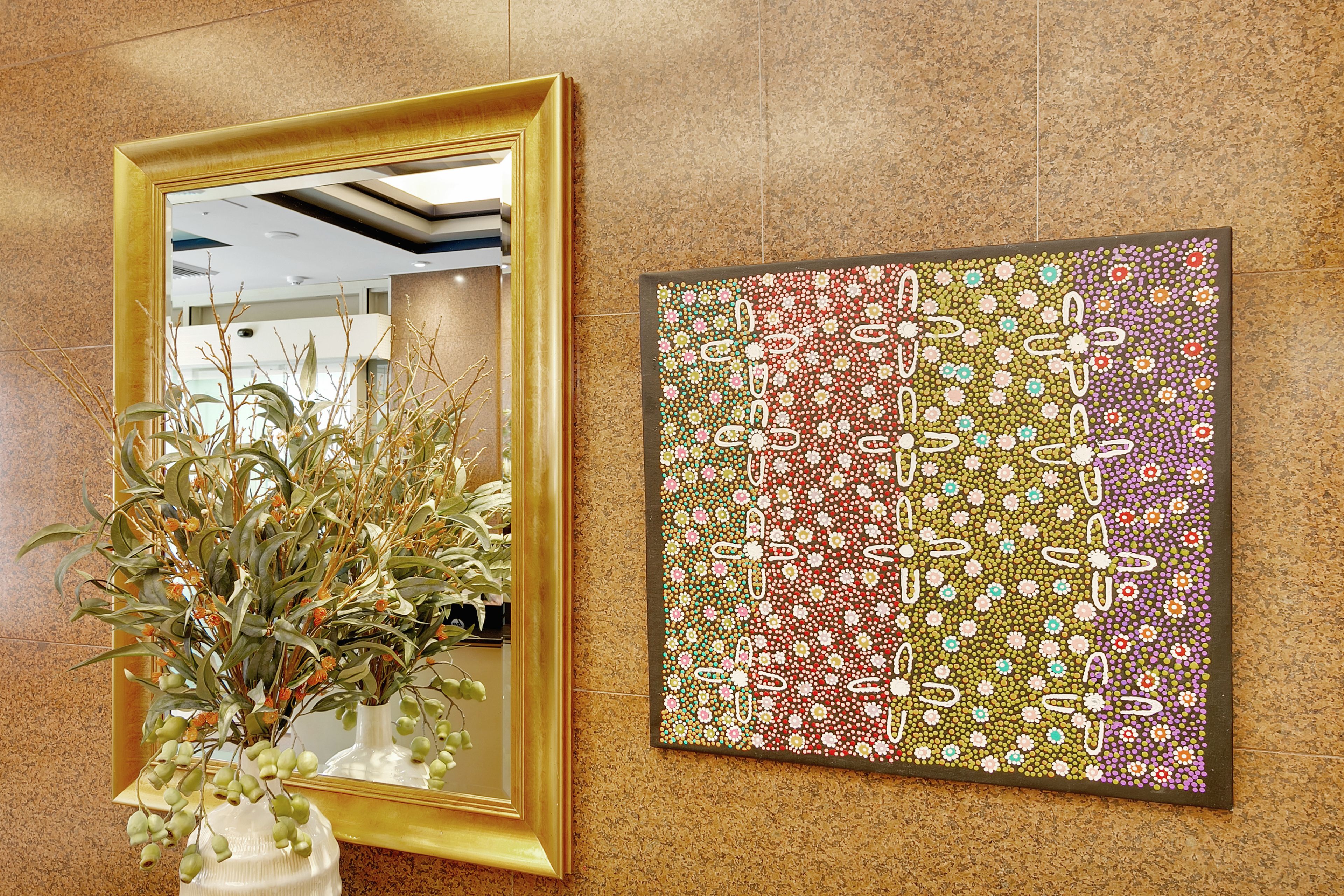 A framed mirror with a plant beside it and a colorful abstract painting on the wall.
