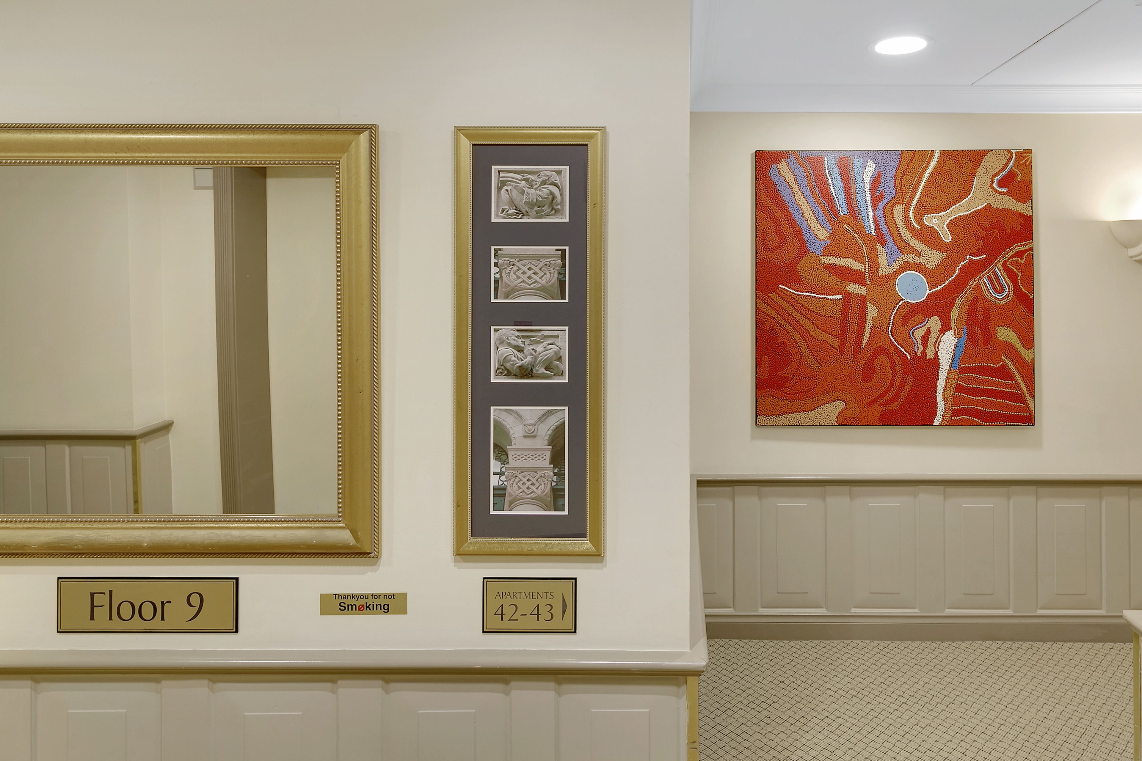 A hotel corridor with a large mirror, framed artwork, and a sign indicating "Floor 9" and "Apartments 42-43".